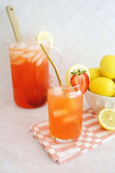 two glasses filled with lemonade and strawberries on a table next to some lemons