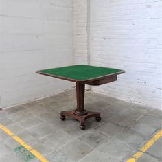 a green table sitting on top of a cement floor next to a white brick wall