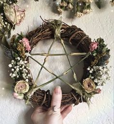 a hand holding a wicker pen over a wreath with flowers and leaves on it