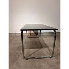 a black table sitting on top of a cement floor next to a white wall in an empty room