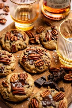 chocolate chip cookies with pecans and caramel are on a cutting board next to two glasses of whiskey