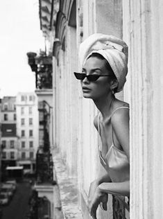 a woman wearing sunglasses and a towel on her head leaning against a wall in the city