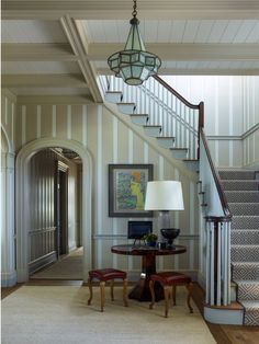 a room with a table, chair and lamp on the floor in front of stairs