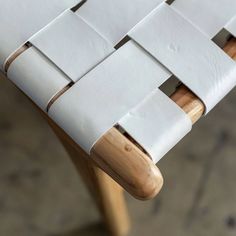 a close up of a white chair with wooden legs and straps on the backrest