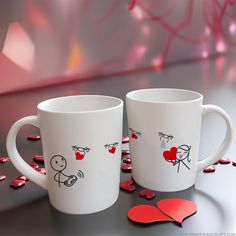 two coffee mugs sitting next to each other on a table with hearts around them