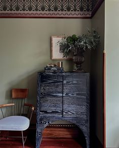 a room with a chair, table and vase on top of the dresser in it