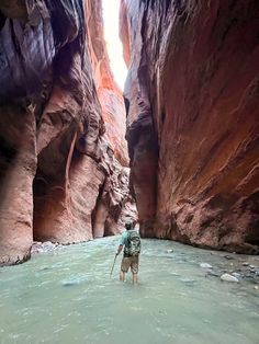 a man is wading through the water in a narrow canyon