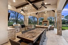 an outdoor kitchen and dining area with stone walls, ceiling fans, and wood table