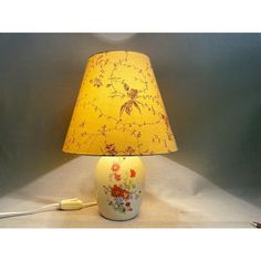 a yellow lamp with flowers on it and a cord plugged into the light bulb