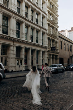 the bride and groom are walking down the cobblestone street in front of tall buildings