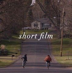 two bicyclists riding down the road in front of a house with short film written on it