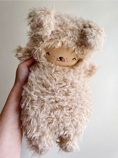 a hand holding a stuffed animal in front of a white wall