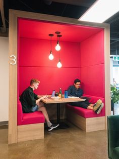 two young men sitting at a table in a room with bright red walls and flooring