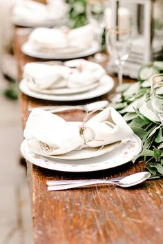 the table is set with white plates and silverware, greenery, and candles