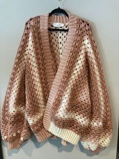 a pink and white crocheted sweater hanging on a wall next to a hanger