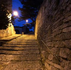 an alley way with cobblestone stone walls and street lights on either side at night