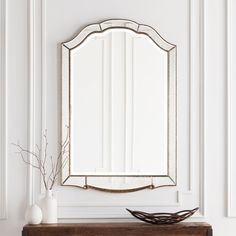 a mirror sitting on top of a wooden table next to a vase with flowers in it