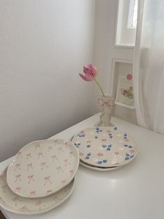 two plates and a vase with a flower in it on a white countertop next to a window