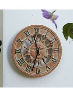 a clock that is on the side of a wall with flowers in front of it