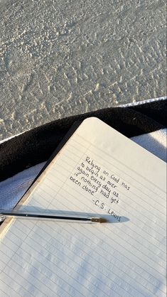 a notepad and pen sitting on top of an open notebook next to the ocean