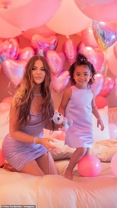 two women sitting on a bed in front of pink balloons and heart - shaped balloons