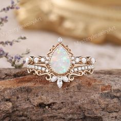 an opal and diamond ring sits on top of a rock next to some flowers