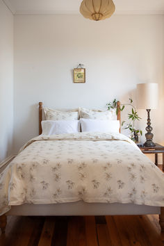 a bed with white sheets and pillows in a bedroom next to a lamp on a table