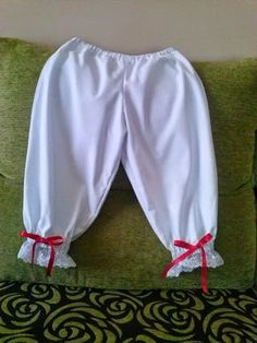 a green pillow with white pants and red ribbon on the bottom, sitting on a bed