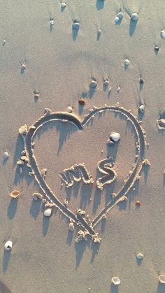 a heart drawn in the sand with shells