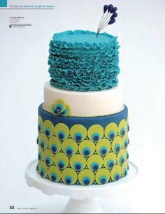 a three tiered cake decorated with blue and green decorations on a white pedestal,