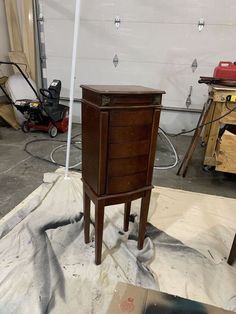 a small wooden cabinet sitting on top of a piece of cardboard in a room filled with tools