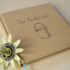 an open book with a flower on it and the words our bucket list written in cursive ink