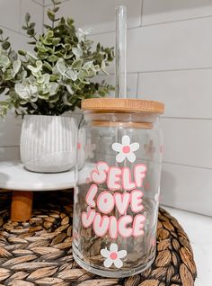 a clear jar with pink and white flowers painted on it sitting on a table next to a potted plant