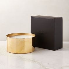 a gold candle sitting next to a black box on a white counter top with the lid open