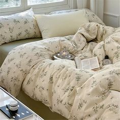 an unmade bed sitting in front of a window next to a book and cup