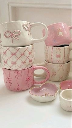 a stack of pink and white ceramic cups with bows on them, sitting next to each other