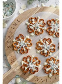 six pretzels are arranged on a wooden platter with white frosting and sprinkles