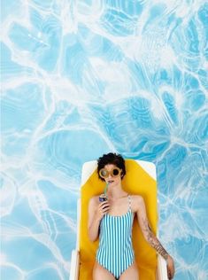 a woman in a blue and white striped swimsuit sitting on a yellow lounge chair