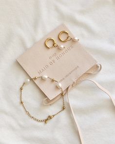 two pieces of jewelry are laying on top of a white sheet with a card attached to it