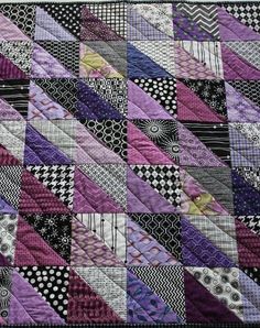 a patchwork quilt is hanging on the wall in front of a white wall with black and purple designs