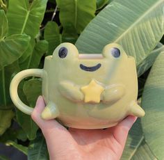 a hand holding a green frog mug with a star on it's face and eyes