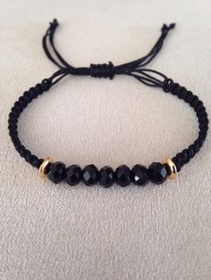 a black beaded bracelet with gold beads on a white cloth covered surface, close up