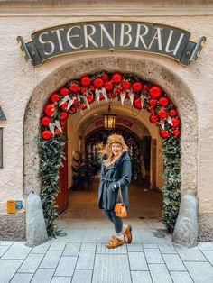 a woman standing in front of a building with red roses on the arch and decorations around it