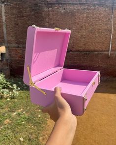 a hand holding a pink box with gold handles