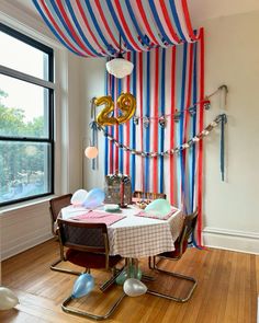 a dining room table with balloons and streamers on the wall next to it in front of a large window