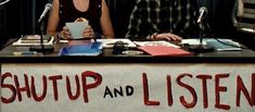 two people sitting at a table in front of microphones with the words shut and listen written on it