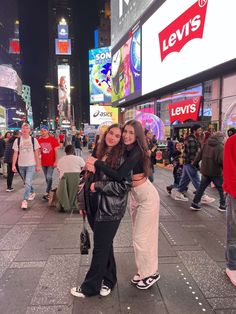 two women are hugging on the street in times square