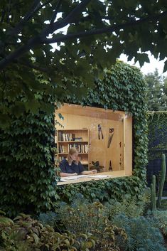 two people are sitting in an open bookcase surrounded by greenery