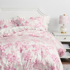 a bed with pink flowers on it in a white room next to a night stand