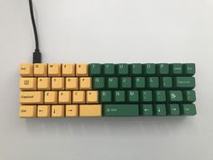 a yellow and green computer keyboard sitting on top of a white table next to a black cord